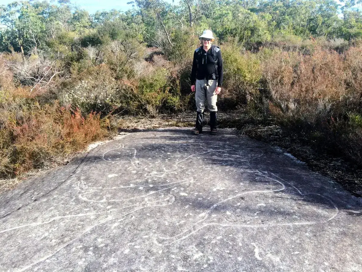 Hiker stands beside ancient Aboriginal rock engravings on the Mill Creek walk
