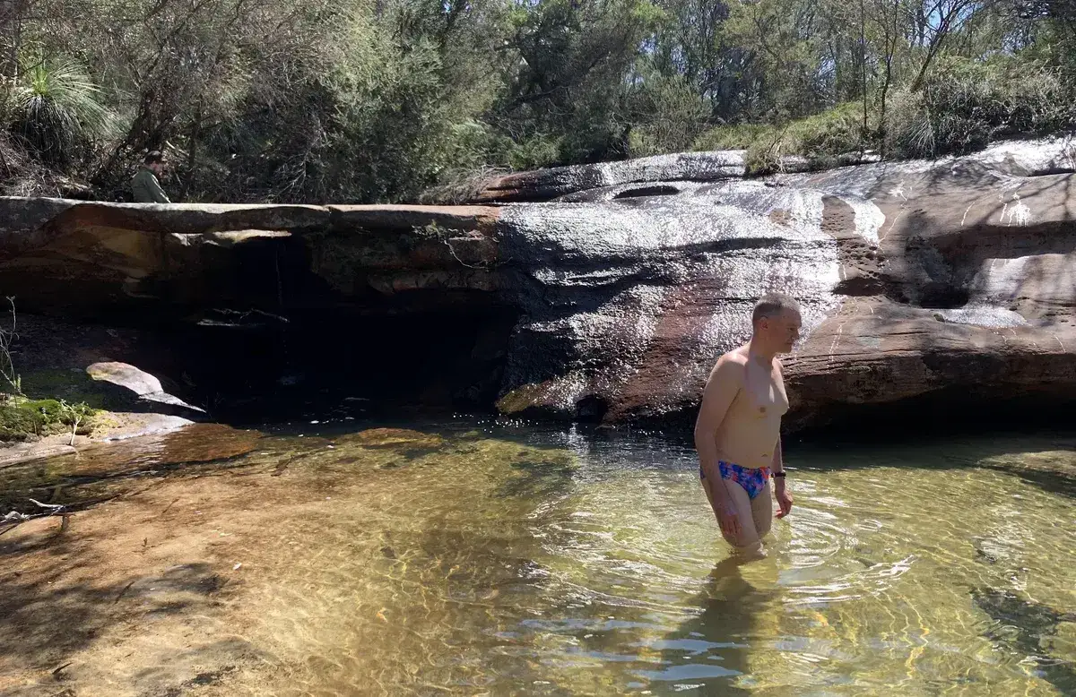 Hiker wading through a tannin pool beneath a rock overhang near Tank Cove