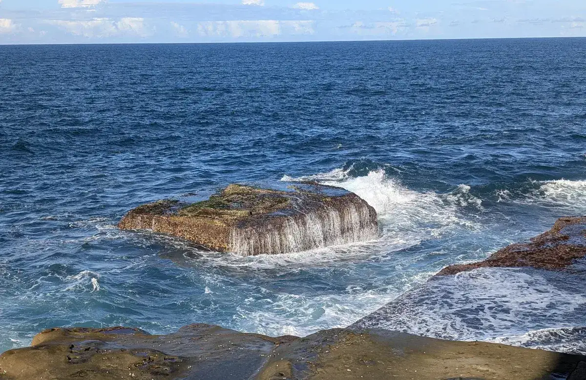 Waves crashing over a large rock just offshore at Winney Bay