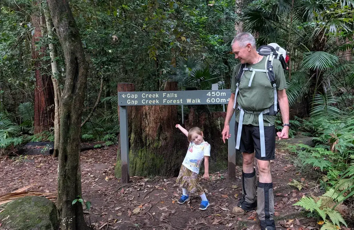 Hiker and toddler pause at the Gap Creek Falls trail sign in the rainforest