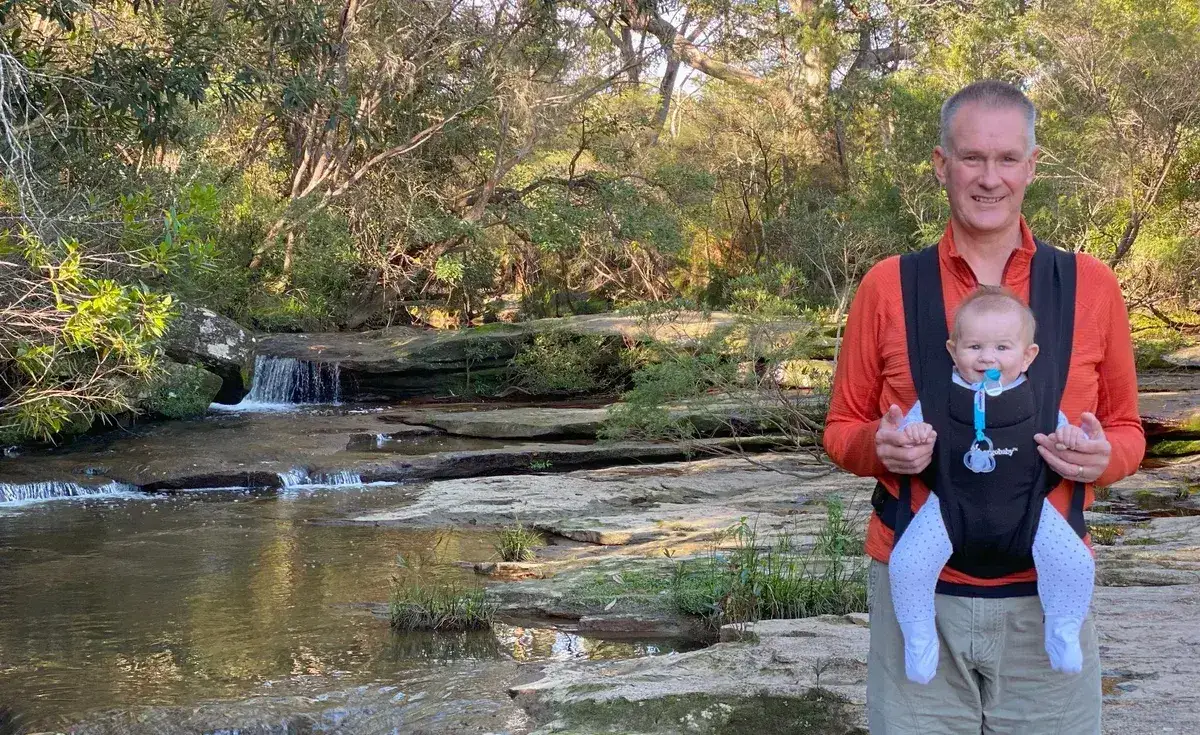 Father with a baby carrier standing beside a small waterfall on Girrakool creek