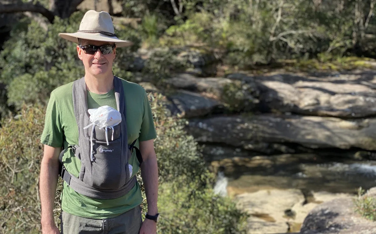 Hiker in a wide brim hat pauses beside Girrakool creek on the loop track