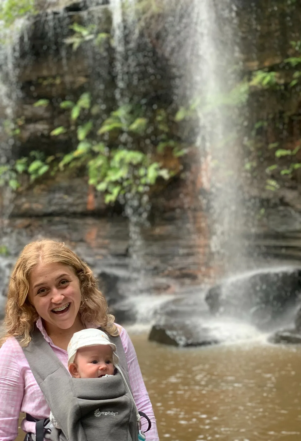 Mother and baby in a carrier smiling in front of a fast flowing Girrakool waterfall