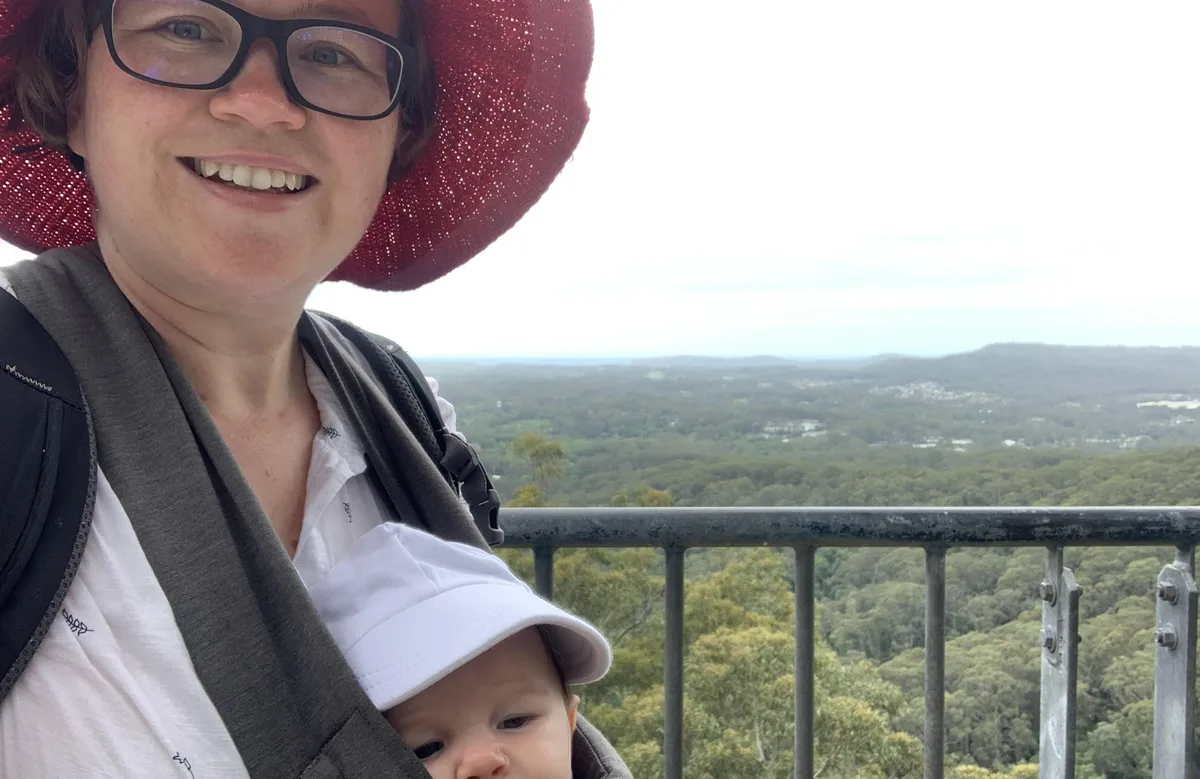 Hiker in a red hat carries a baby at a bush lookout over Rumbalara