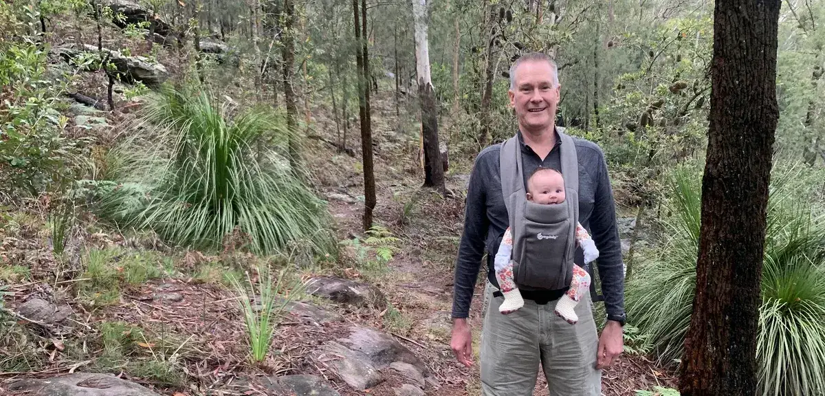 Hiker carries a baby past grass trees on the Gosford to Lisarow trail