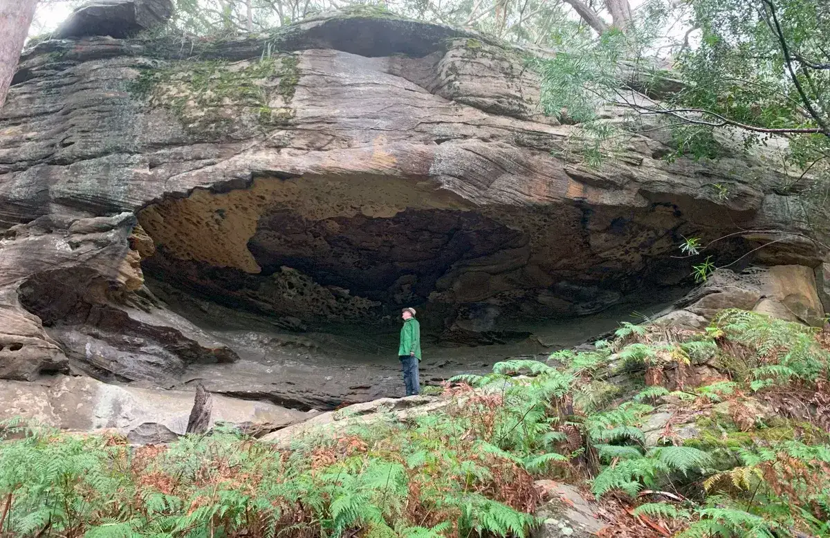 Hiker standing inside a large sandstone rock shelter on the ridge trail