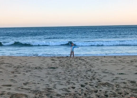 Walker throwing arms up on the sand at Killcare Beach with waves rolling in