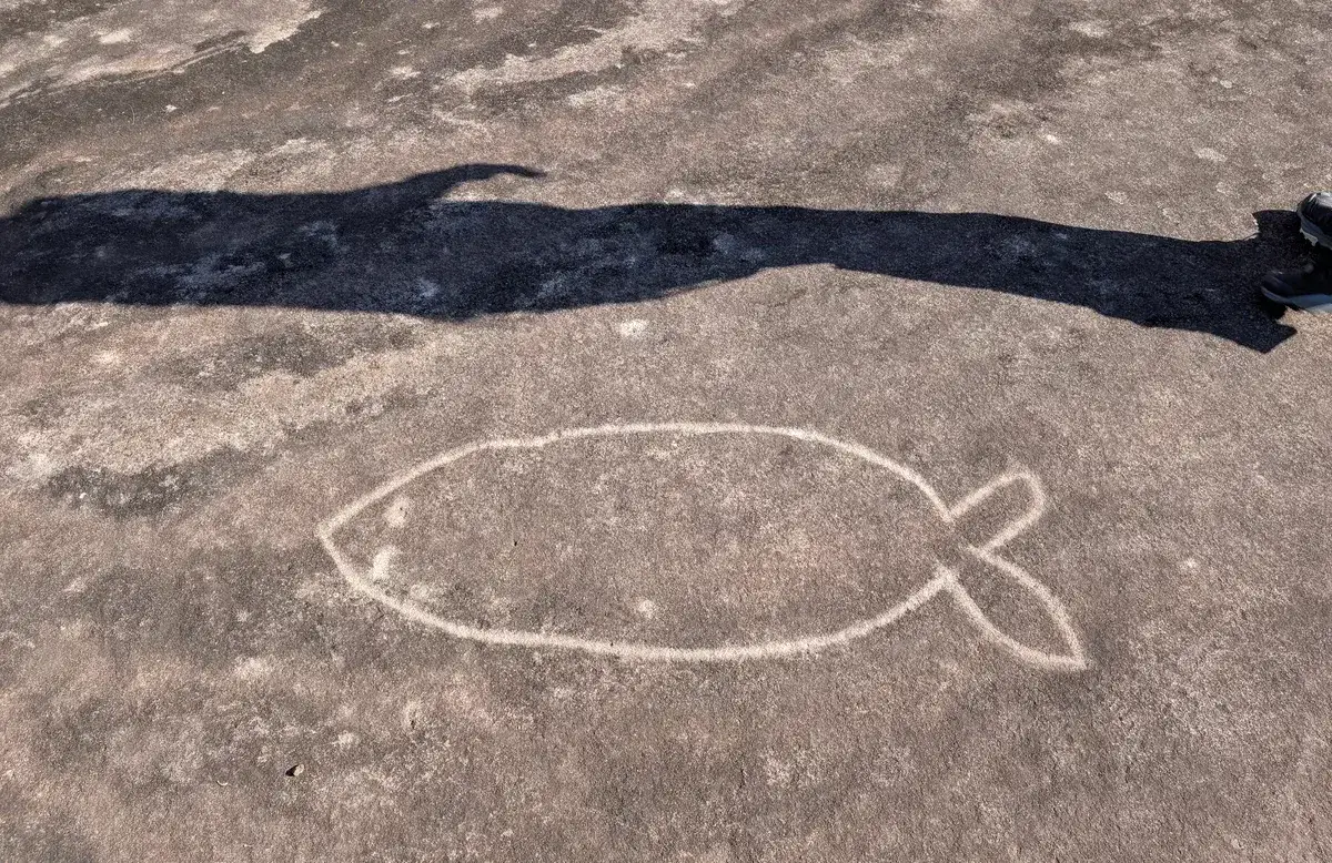Fish shaped rock engraving with a hiker's shadow stretching across it