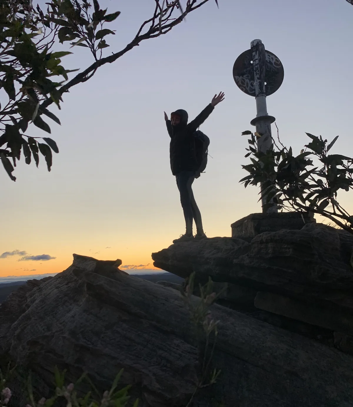 Hiker celebrating atop Mount Wondabyne beside the summit trig marker at sunset