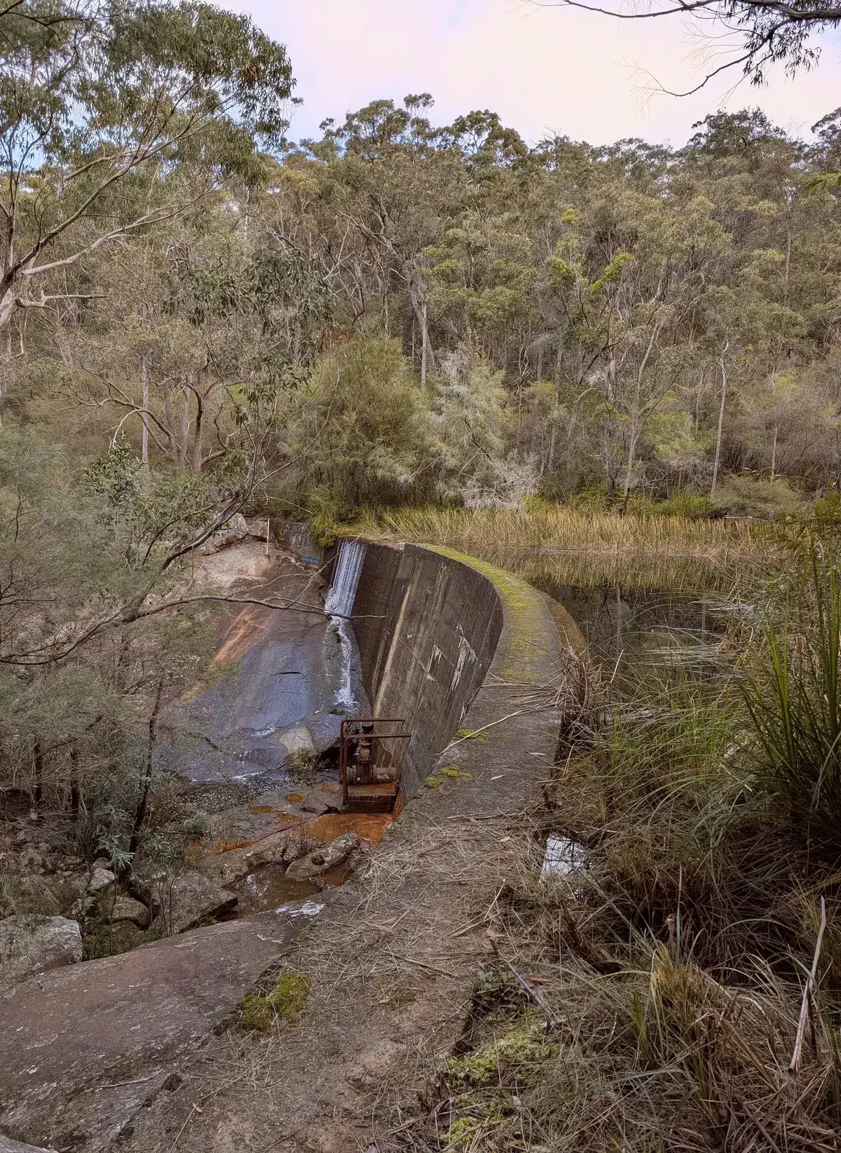 Concrete wall of the old Narara railway dam with water trickling over the spillway