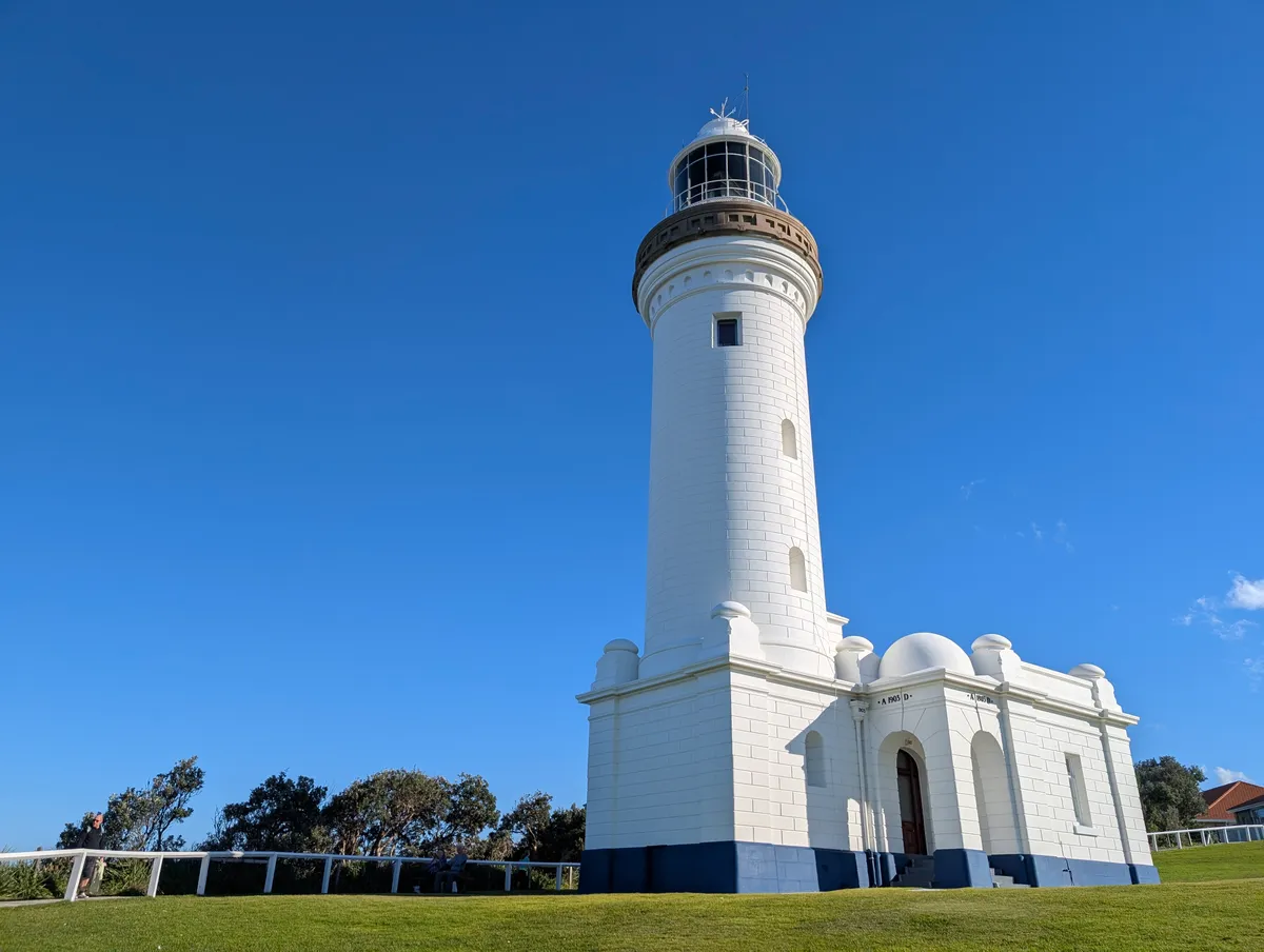The white Norah Head Lighthouse tower, built in 1903, against a clear blue sky on the grassy headland