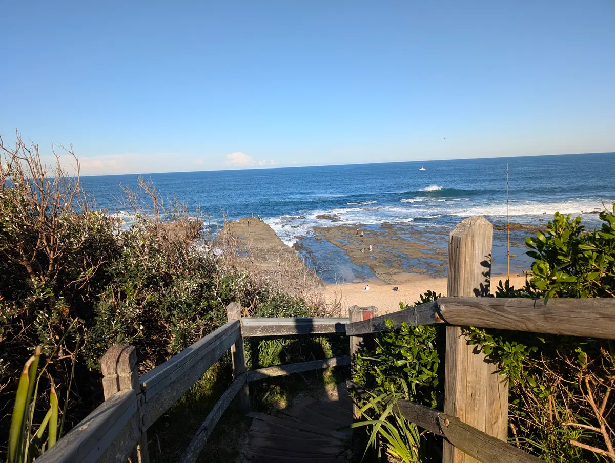 Timber stairs and railing leading down through coastal scrub to the rock platform and beach below Norah Head