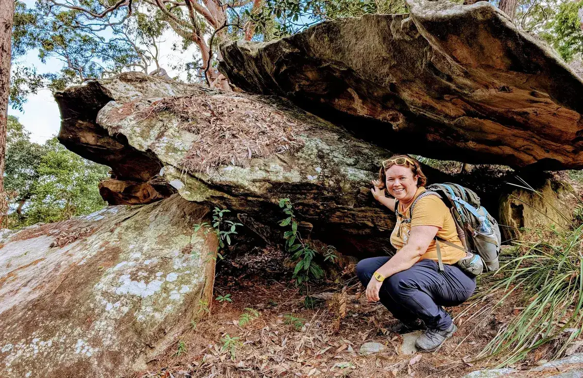 Hiker crouching beneath a low sandstone overhang smiling