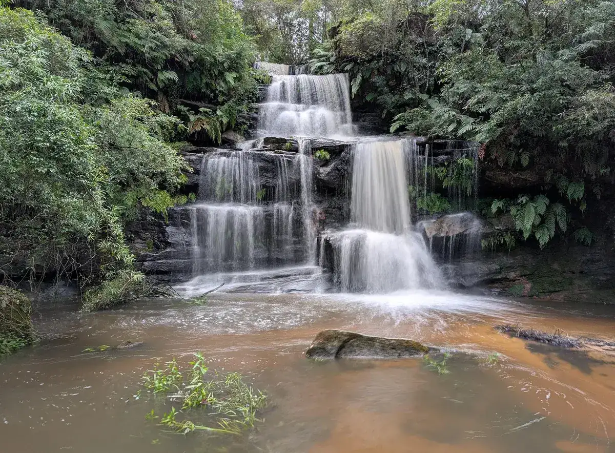 wide view of Ironbark Falls tumbling over multiple rock tiers into a tea coloured pool