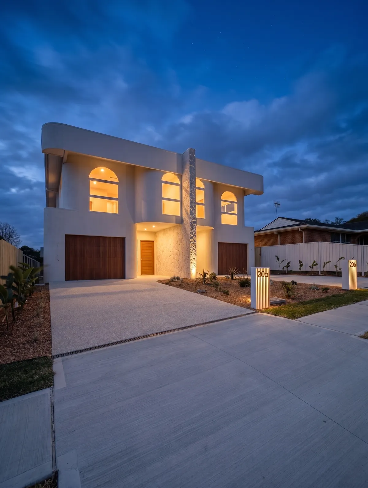 The stone blade wall dividing the two entries, lit against the render at dusk