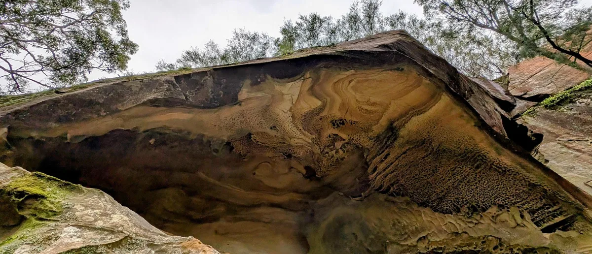 swirling honeycombed sandstone overhang with ochre and grey rock banding