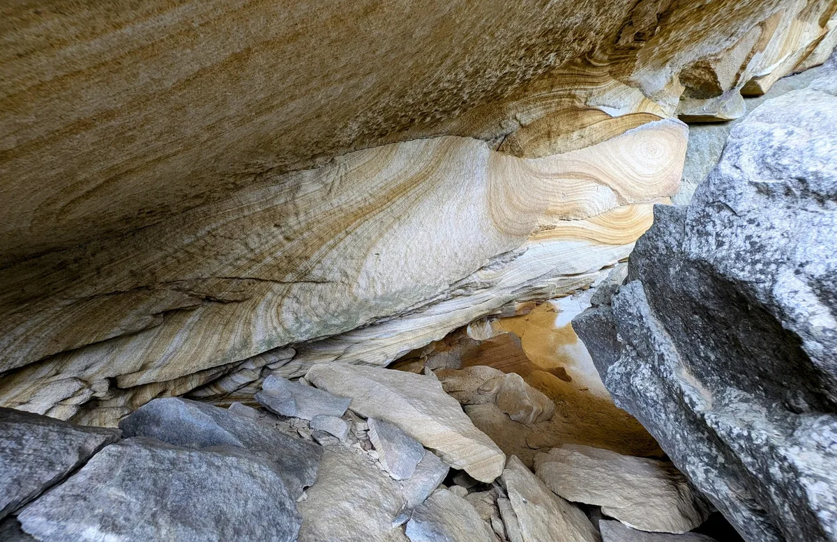 swirling banded sandstone ledge above jumbled grey boulders in a rock shelter