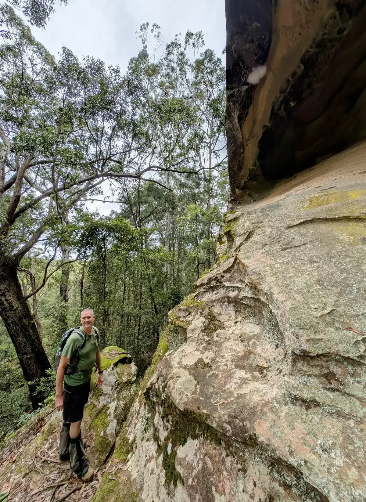 Hiker smiles on a narrow ledge below a honeycombed overhang