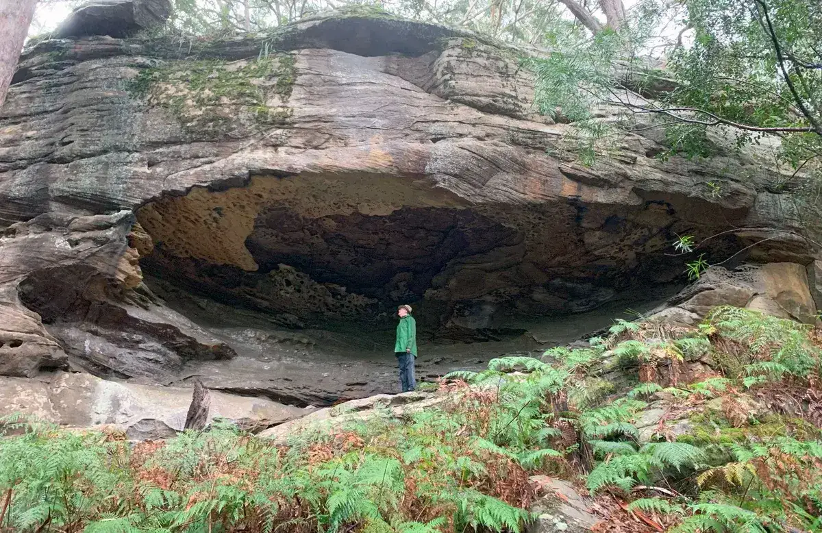 Hiker dwarfed inside a large sandstone rock shelter
