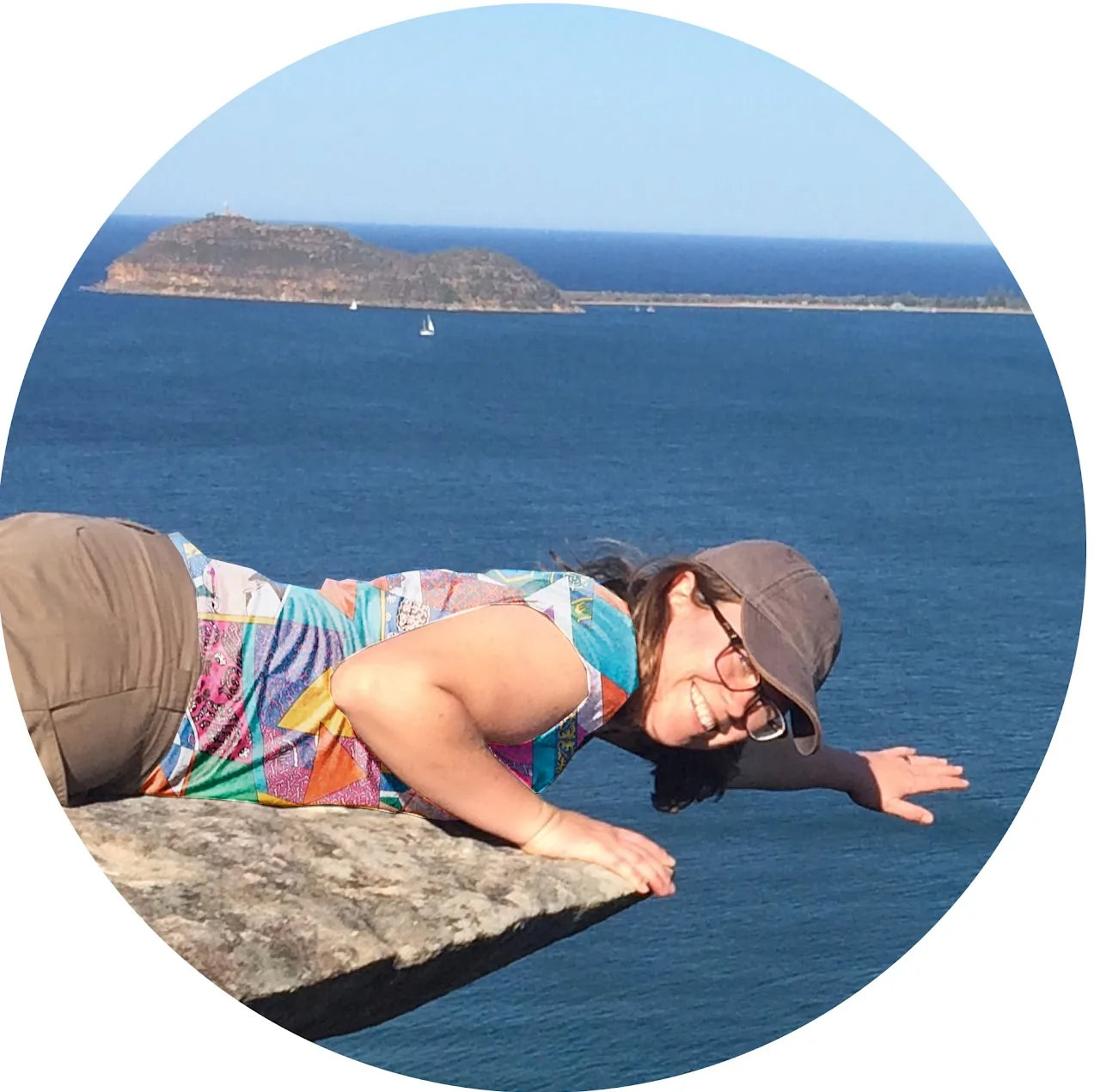 Woman lying flat on a clifftop rock overlooking the ocean and islands
