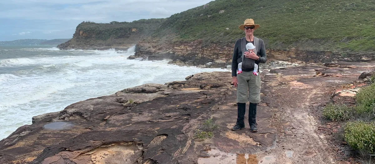 hiker carrying a baby in a carrier on the rocky Tallow Beach headland