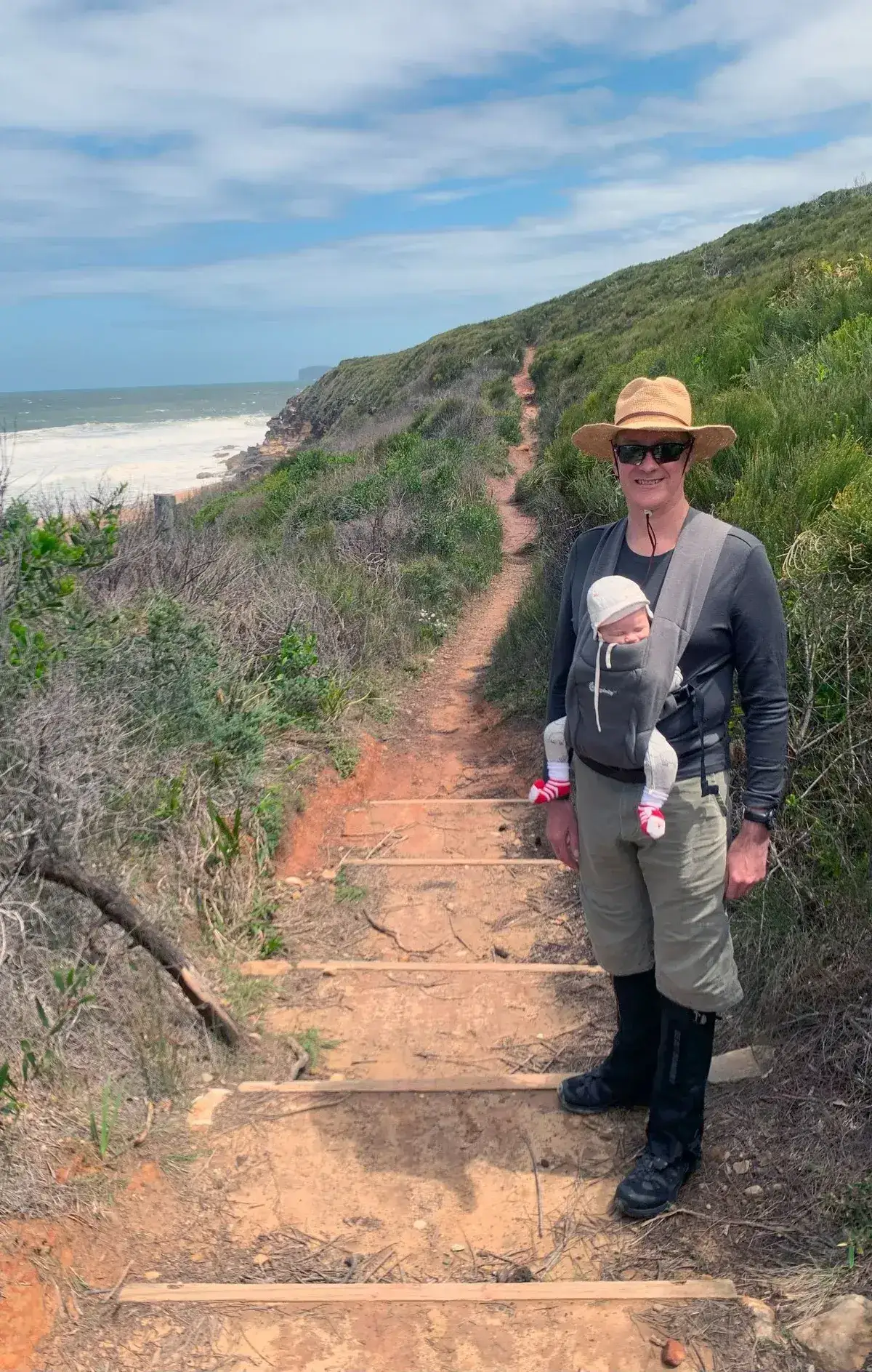 hiker with baby carrier descending timber steps on the steep Tallow Beach track