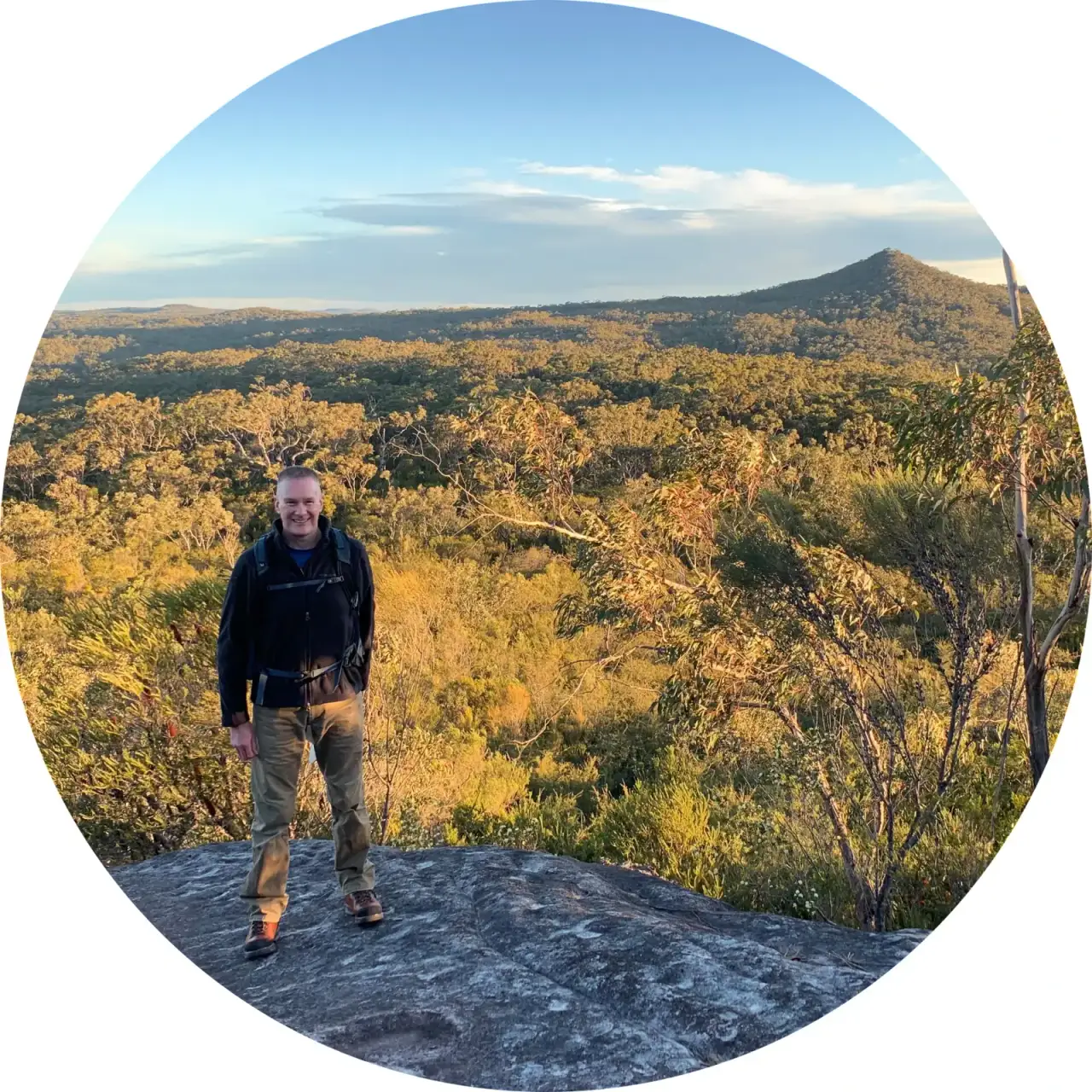 Man standing on a rock ledge overlooking bushland at sunset
