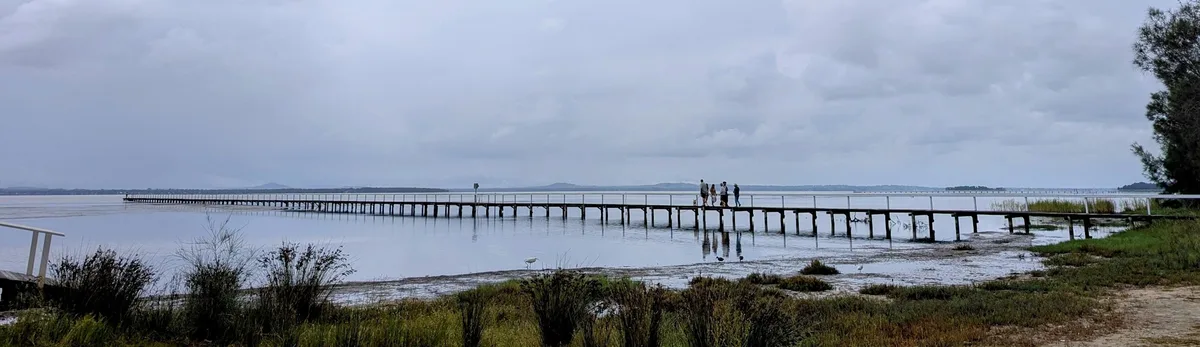 long timber jetty stretching over Tuggerah Lake with people walking