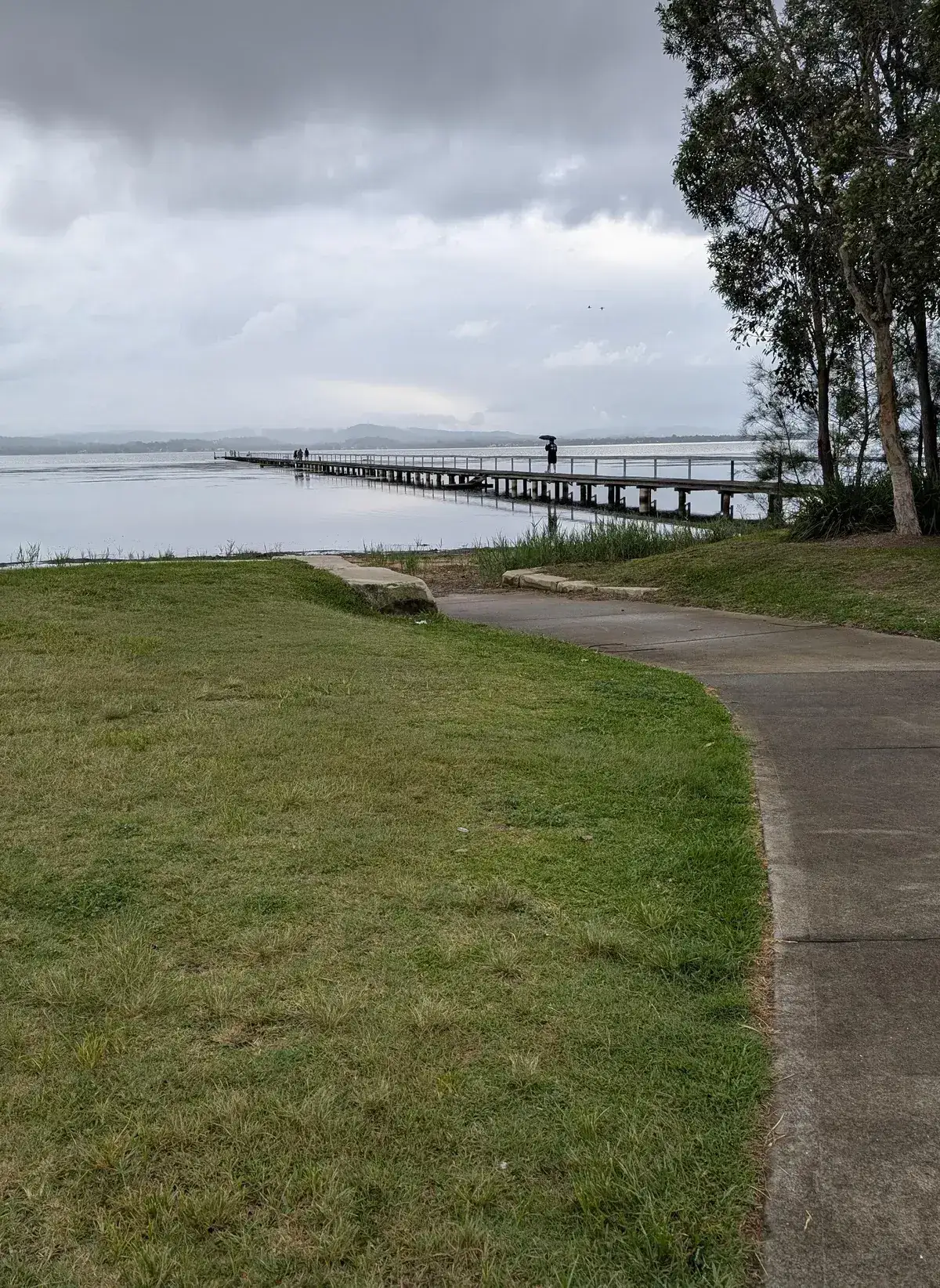 person with an umbrella walking along a long timber jetty over the lake