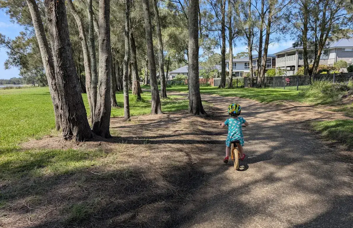 child on a balance bike riding a grassy tree lined path near homes