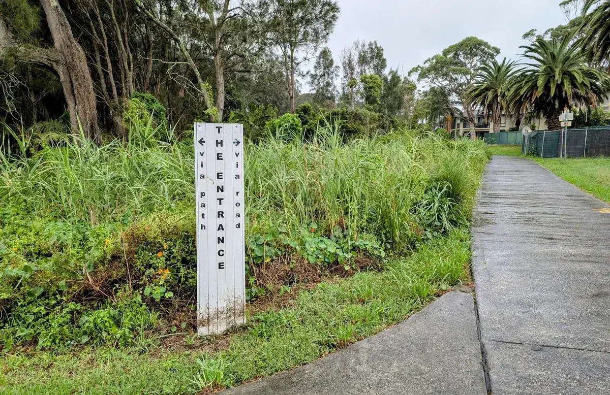 The Entrance directional signpost among grasses beside the shared path