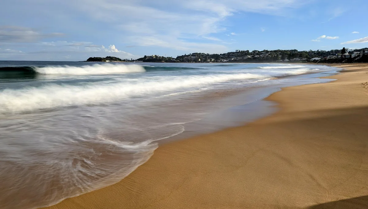 Wave breaking on the shore at Wamberal Beach with houses on the hill